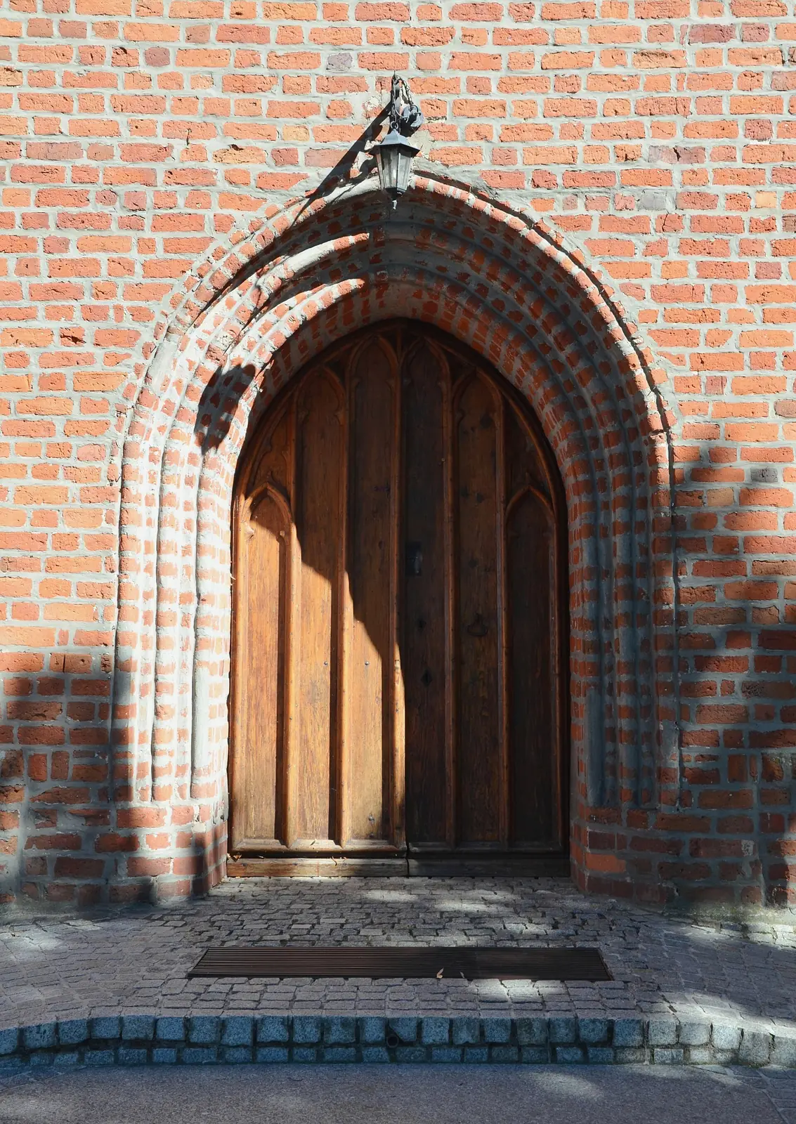 Ostrołukowy gotycki portal z ceglanym obramieniem i drewnianymi drzwiami